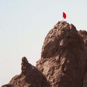 Berggipfel mit roter Fahne – Symbolbild für das Bewältigen schwieriger Lebensphasen und das Durchhalten in psychischen Krisen.