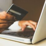 Hand hält Karte vor Laptop – Symbolbild für Psychotherapie-Kosten und Abrechnung mit gesetzlicher Krankenkasse und privater Krankenversicherung